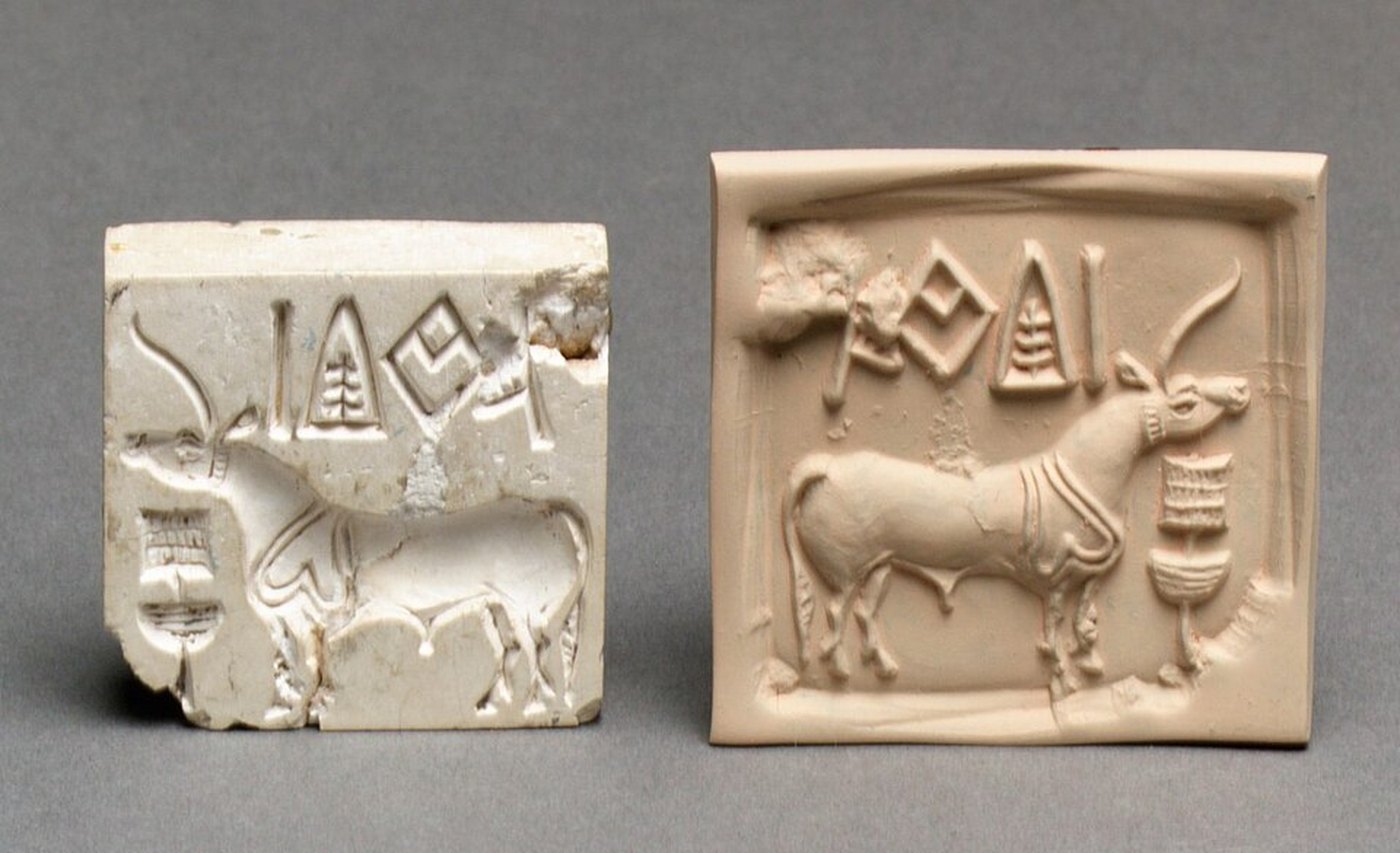 An Indus Valley stamp seal in stone beside its modern clay impression. A row of script signs runs along the top edge above a one-horned bull.